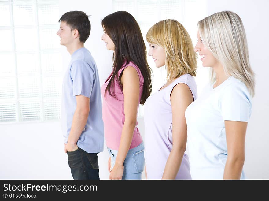 Group of smiling friends standing near window. Focused on two first girls. Side view. Group of smiling friends standing near window. Focused on two first girls. Side view.