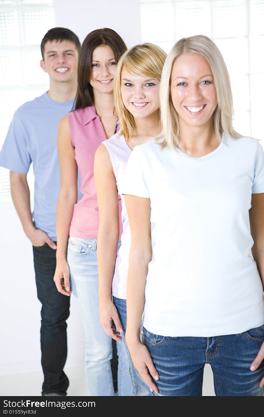 Group of friends standing in the line. They're smilling and looking at camera. Focused on second girl. Front view. Group of friends standing in the line. They're smilling and looking at camera. Focused on second girl. Front view.