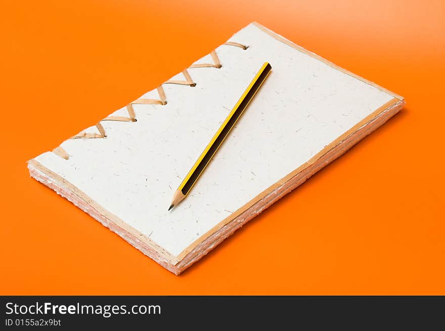 Recycled notepad and pencil over an orange background