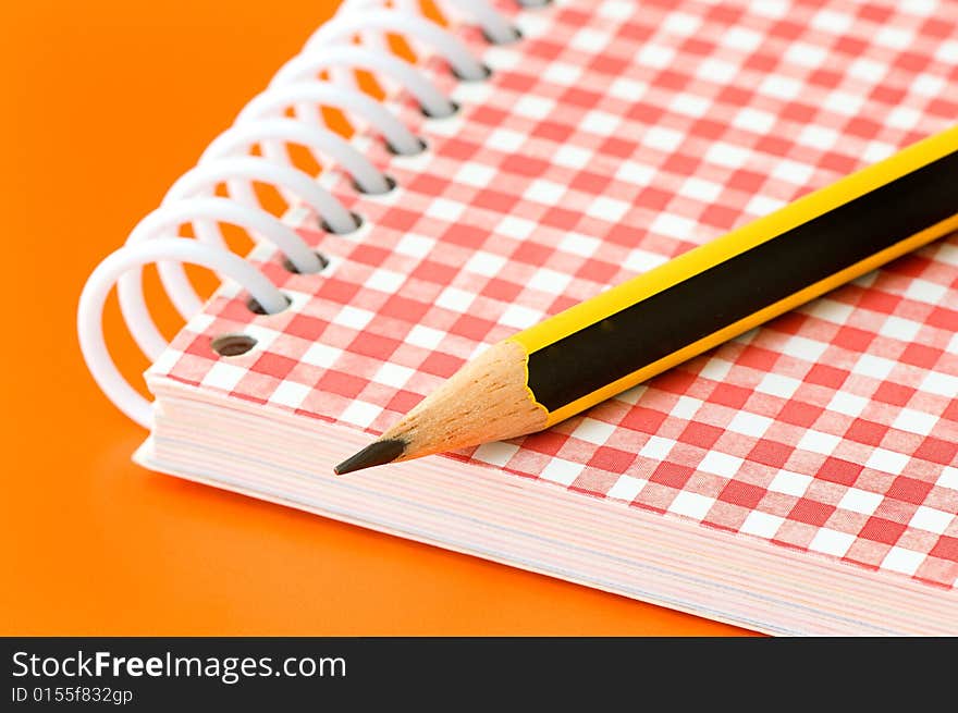 Pencil and notebook over an orange background