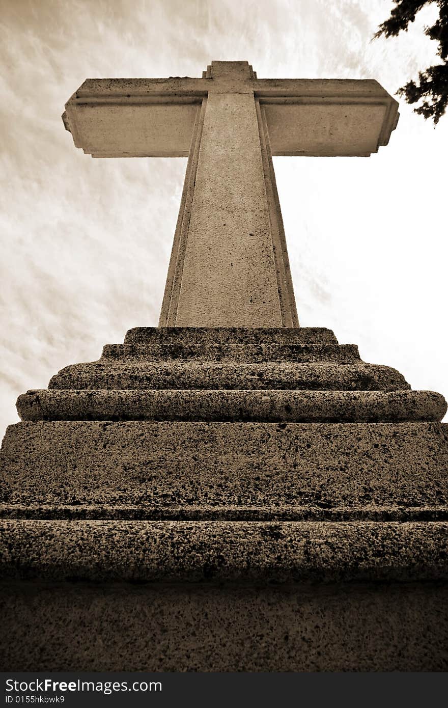 Christian stone cross under cloudscape, sepia toned.