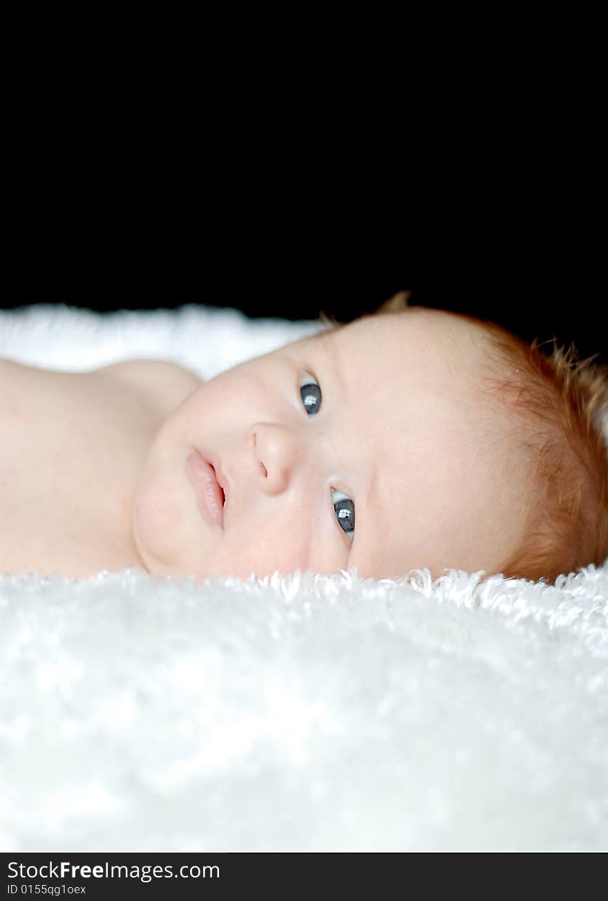 A young baby is laying down in a studio.  He is looking away from the camera.  Vertically framed shot. A young baby is laying down in a studio.  He is looking away from the camera.  Vertically framed shot.