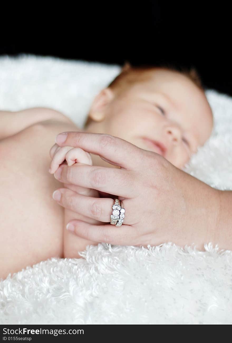 A baby is laying down in a studio. A mother is holding the baby's hand. Vertically framed shot. A baby is laying down in a studio. A mother is holding the baby's hand. Vertically framed shot.