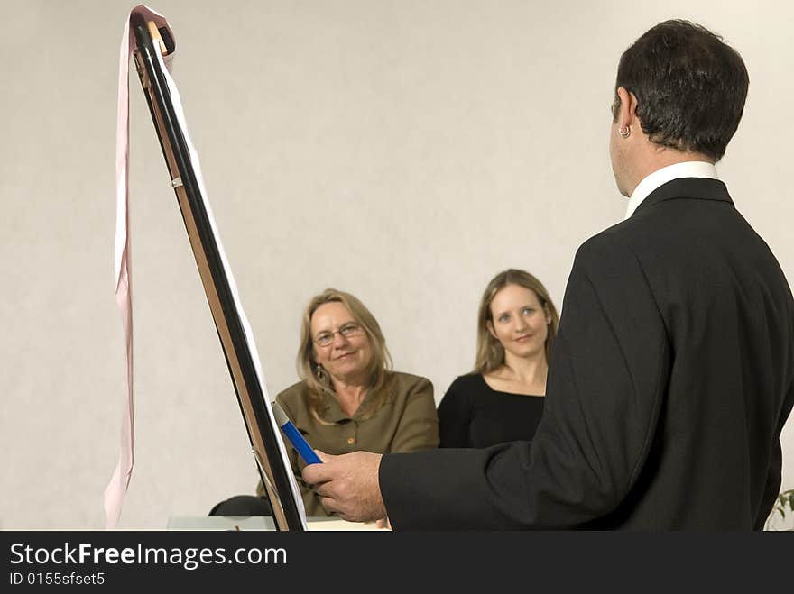 A Boss in instructing his employees in a business meeting. The two girls are smiling at him. Horizontally framed shot. A Boss in instructing his employees in a business meeting. The two girls are smiling at him. Horizontally framed shot.