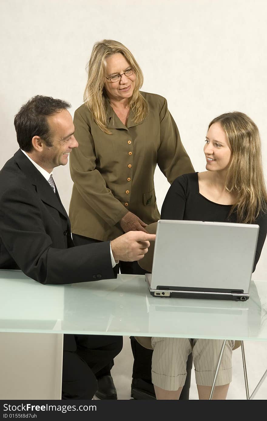 Two women and a man in a meeting at a desk with a laptop. They are all smiling. Vertically framed photo. Two women and a man in a meeting at a desk with a laptop. They are all smiling. Vertically framed photo.