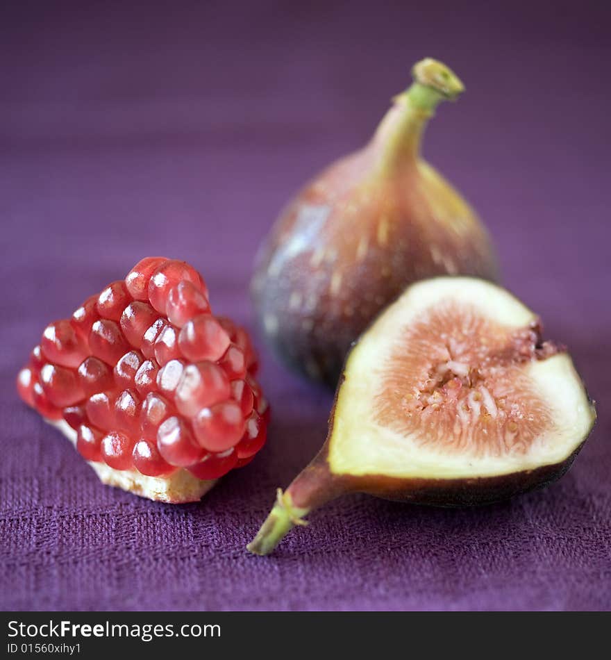 Still life image of a part of pomgranate a whole fig and a slice of fig on purpule cloth. Still life image of a part of pomgranate a whole fig and a slice of fig on purpule cloth