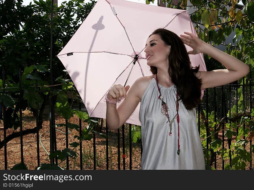 A young brunette beautiful fashion model holding a pink umbrella. A young brunette beautiful fashion model holding a pink umbrella