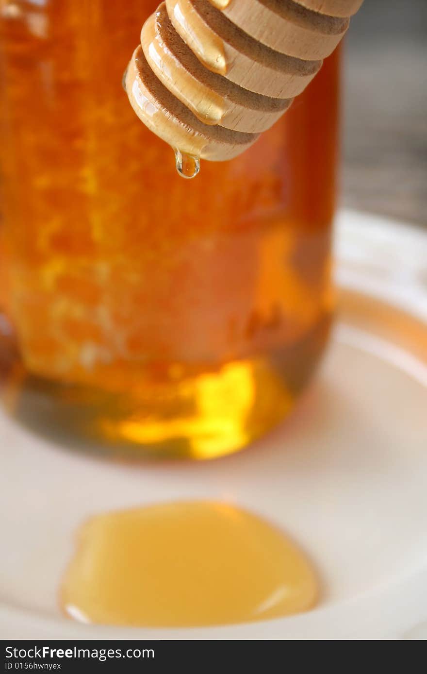 A drop of honey dripping from a dripper. Shallow depth of field and selective focus on the drip and dipper. A drop of honey dripping from a dripper. Shallow depth of field and selective focus on the drip and dipper.