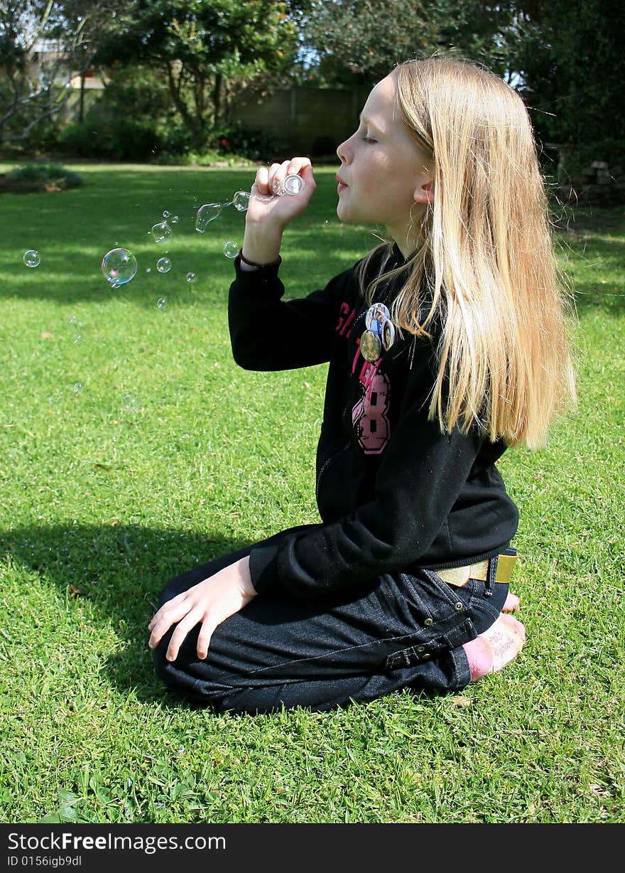 A cute white caucasian girl child sitting in the garden blowing bubbles. A cute white caucasian girl child sitting in the garden blowing bubbles