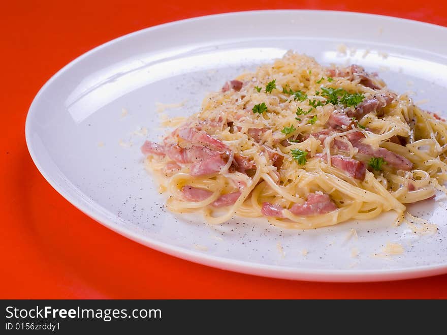 Freshly cooked plate of spaghetti with ham and cheese, decorated with green herbs