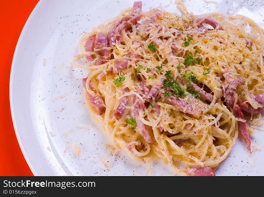 Freshly cooked plate of spaghetti with ham and cheese, decorated with green herbs