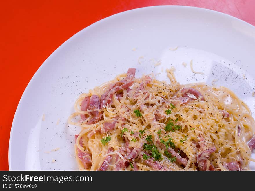 Freshly cooked plate of spaghetti with ham and cheese, decorated with green herbs