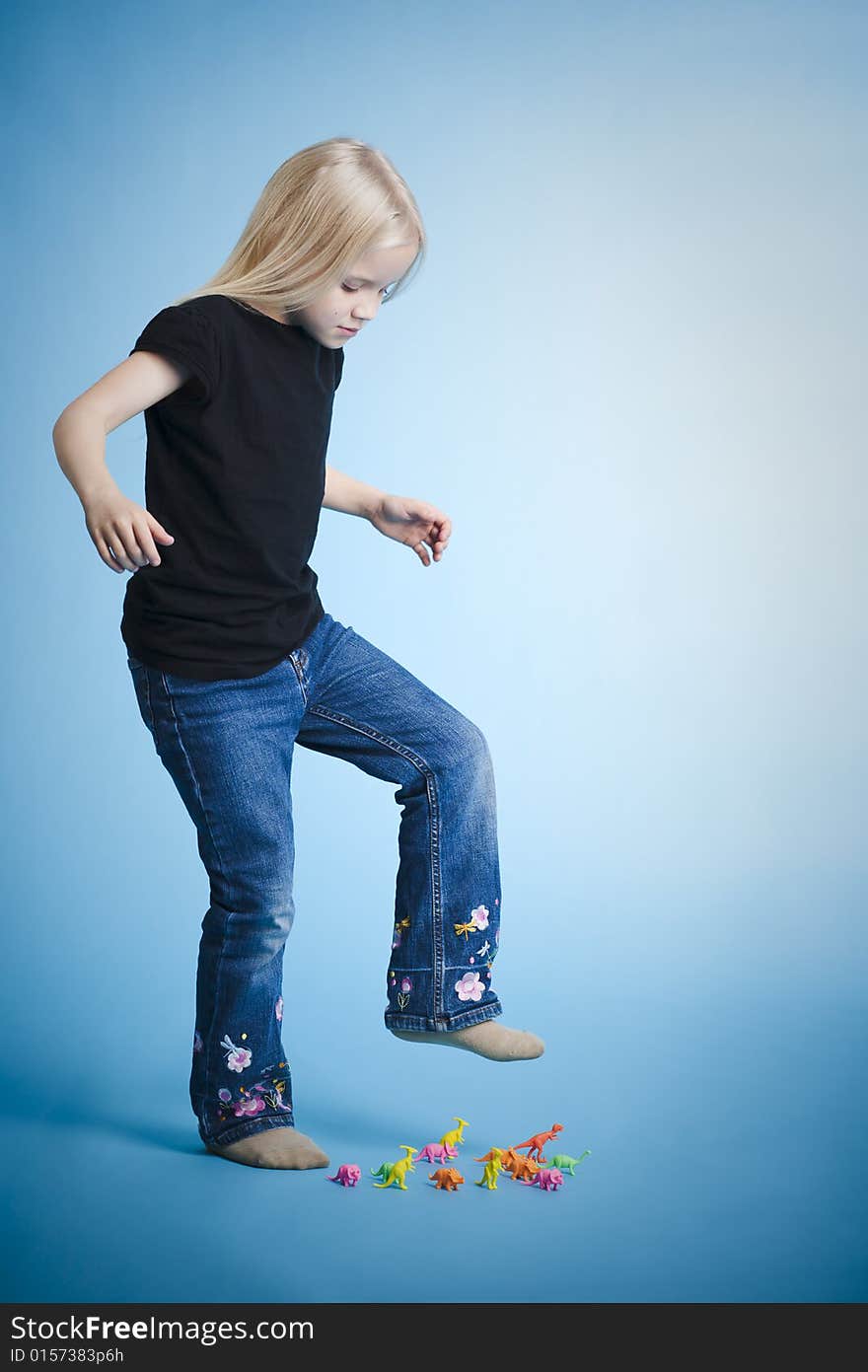 Young girl crushing plastic dinosaurus with her foot. Young girl crushing plastic dinosaurus with her foot