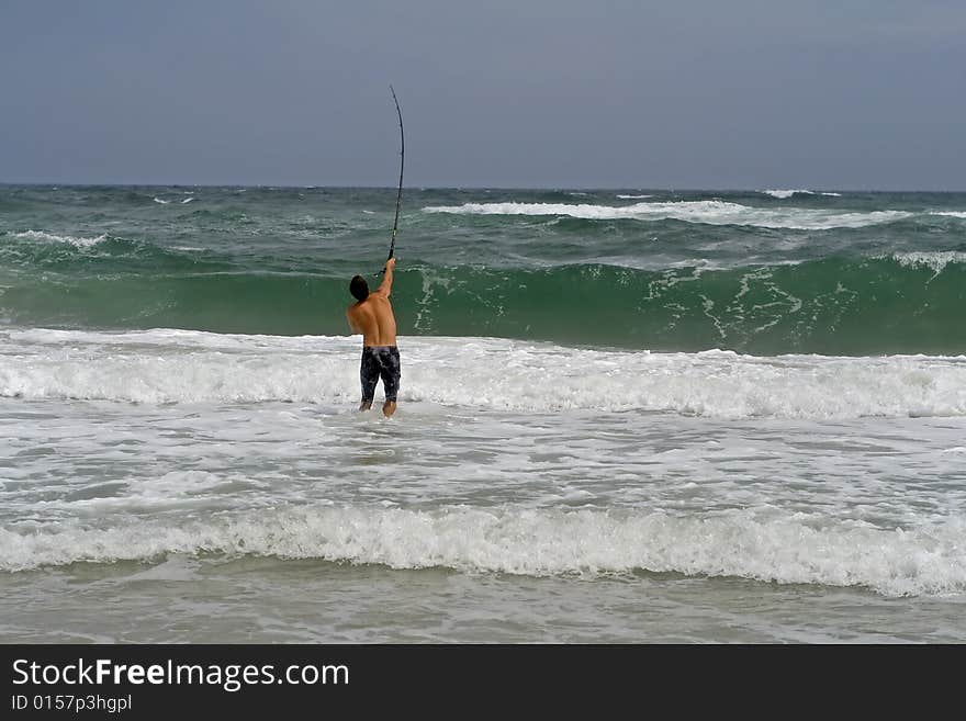 Man surf fishing, casting into the ruff ocean.