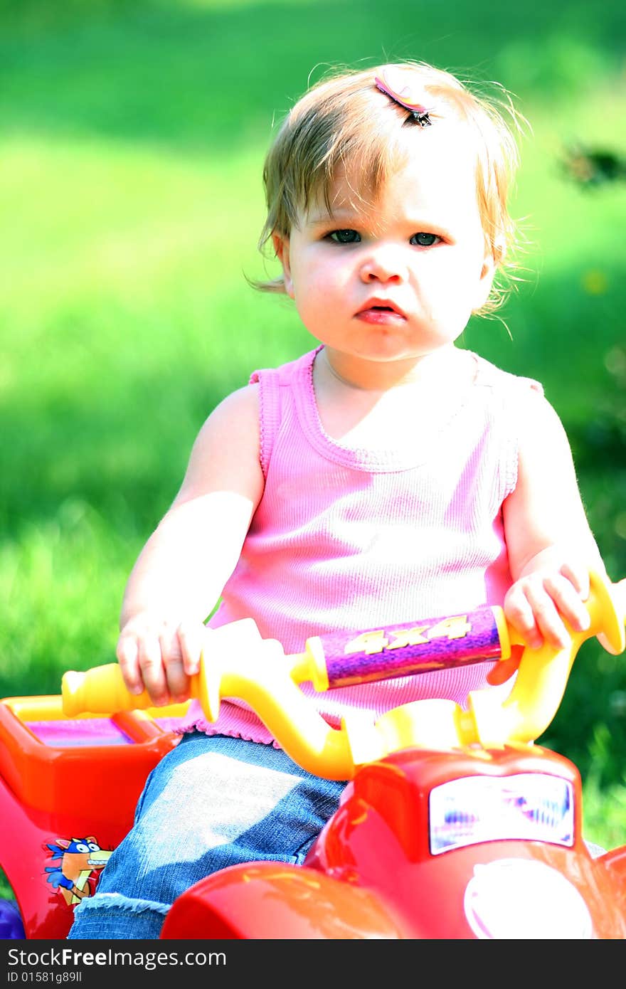 A one year old little girl sits on her toy ATV (All Terrain Vehicle). A one year old little girl sits on her toy ATV (All Terrain Vehicle).