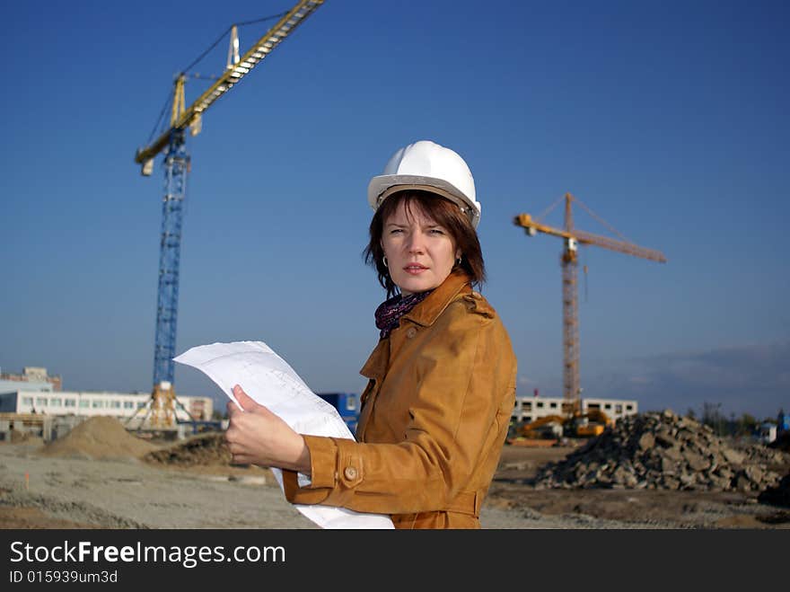 Pretty woman architect holding blueprints and standing in the building site. Pretty woman architect holding blueprints and standing in the building site