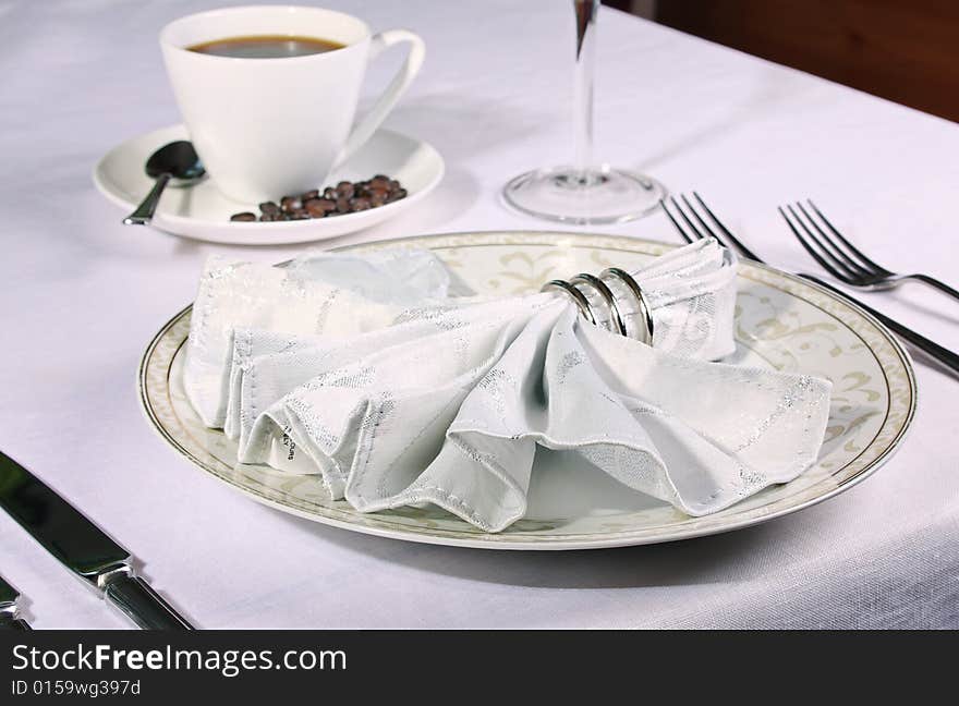 Elegant place setting with piping coffee in background and white fan napkin and ring