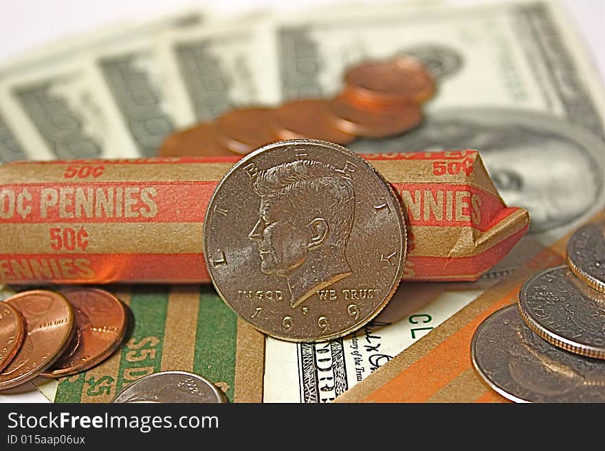 Kennedy half dollar, with pennies, nickels, dimes and quarters, all laid out on money rolls and hundred dollar bills.