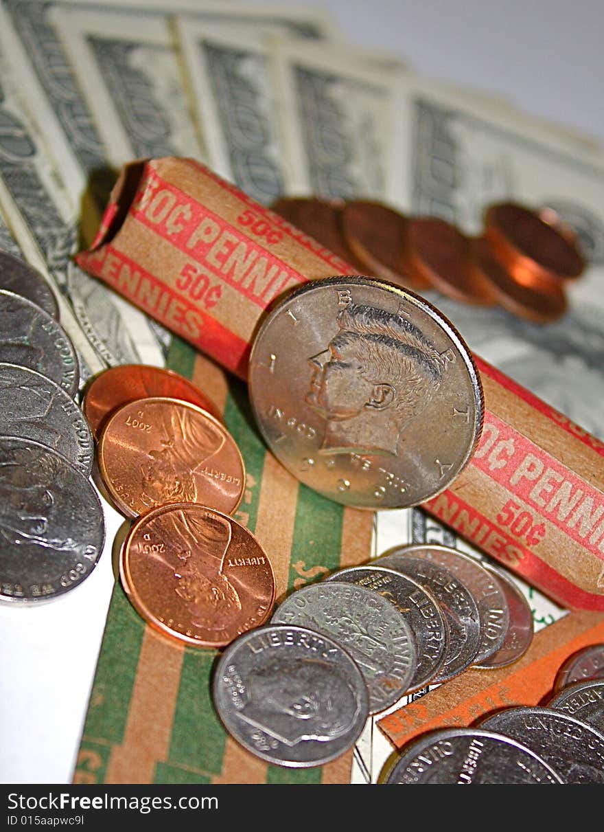 Kennedy half dollar, with pennies, nickels, dimes and quarters, all laid out on money rolls and hundred dollar bills.