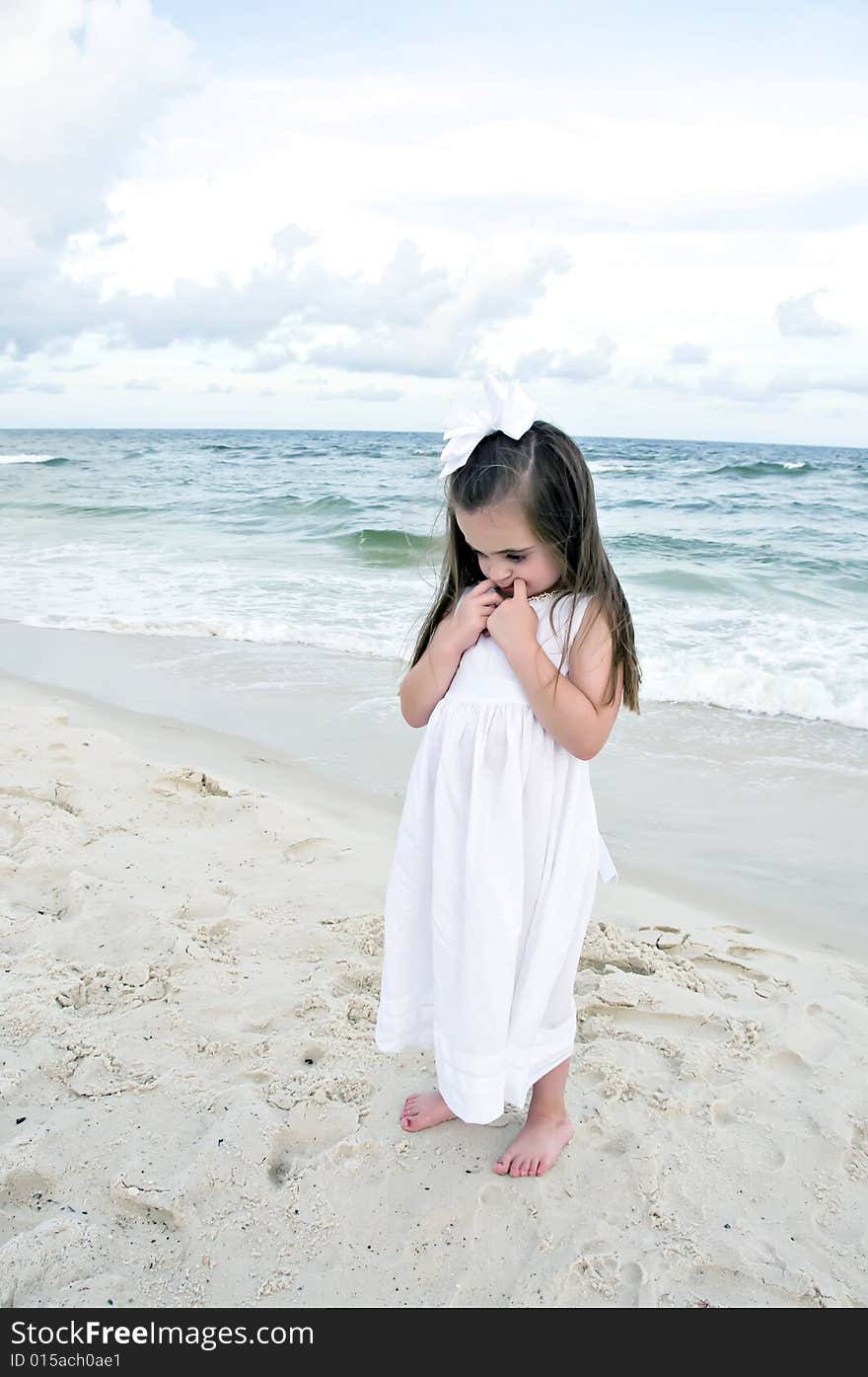 Little girl dressed in white pouting while standing on the beach with the ocean in the background. Little girl dressed in white pouting while standing on the beach with the ocean in the background.