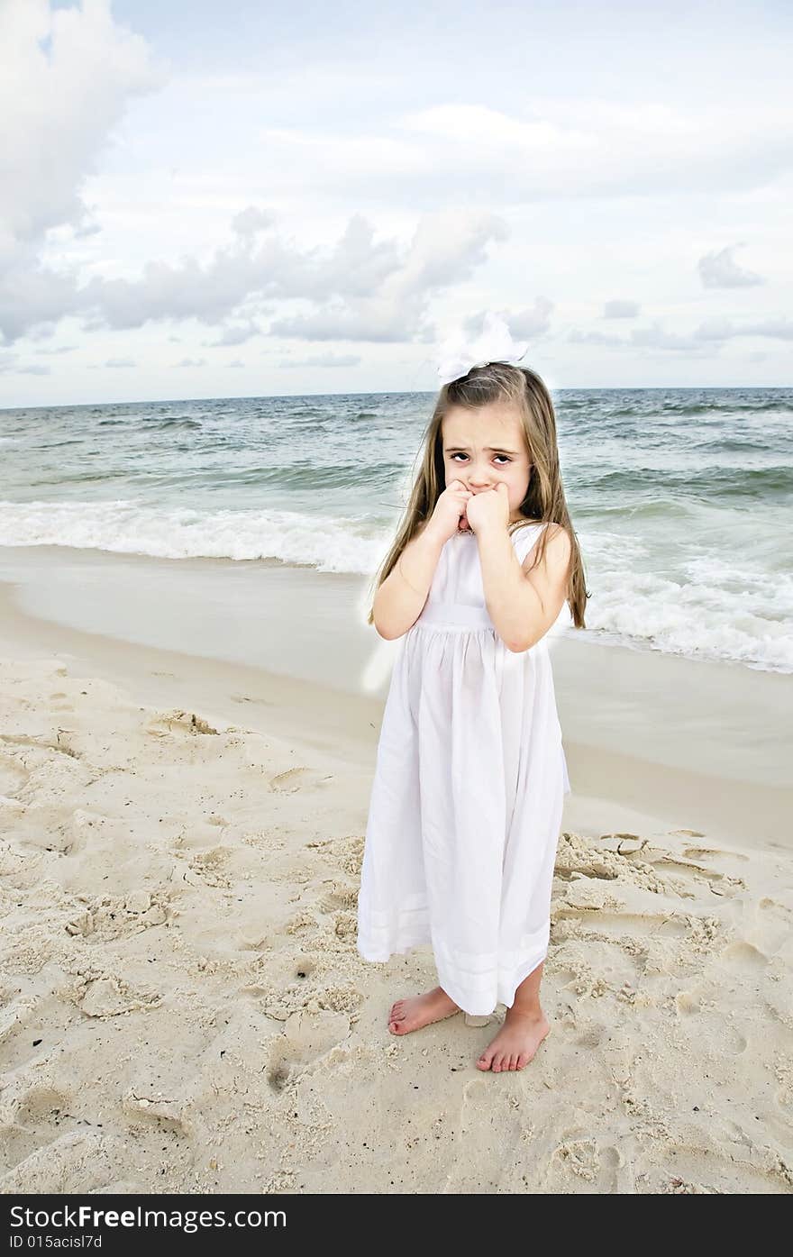 Little girl dressed in white pouting while standing on the beach with the ocean in the background. Little girl dressed in white pouting while standing on the beach with the ocean in the background.