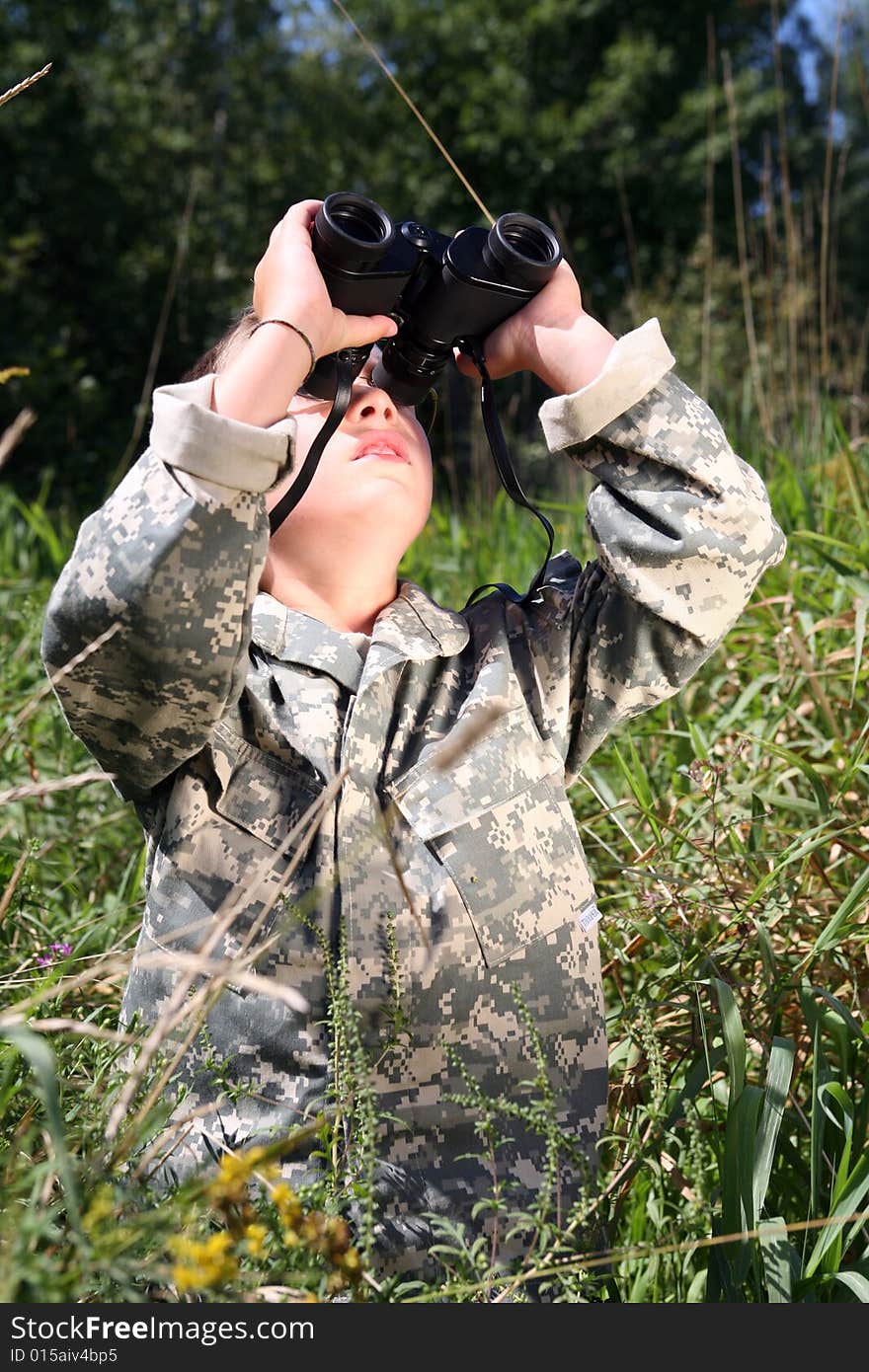 Boy in camouflage looking up through binoculars