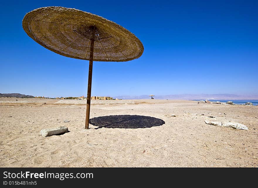 Canopy umbrella parasol shade vertical against a blue sky and sandy beach area.