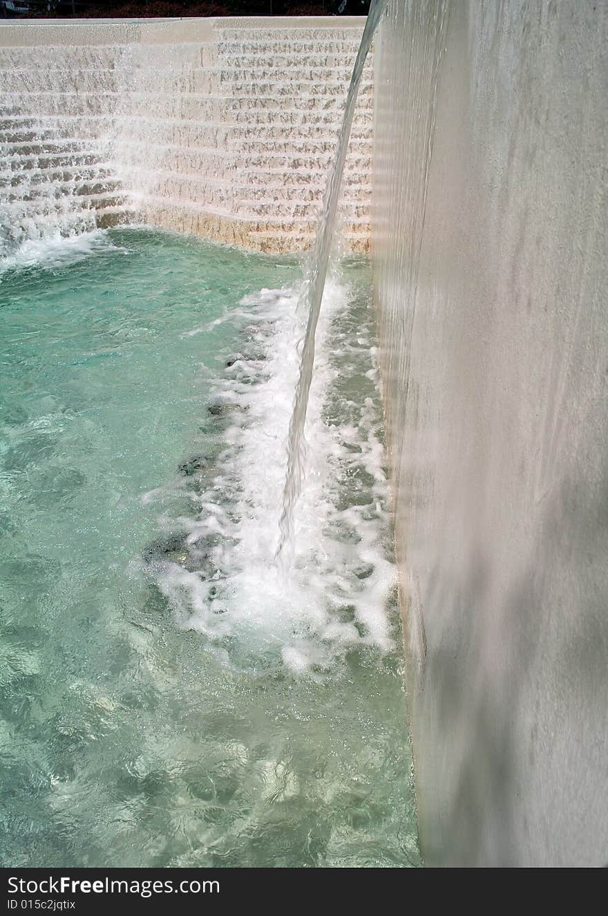 Water flowing down the stairs and over a falls into the cool aqua colored pool of an urban water feature