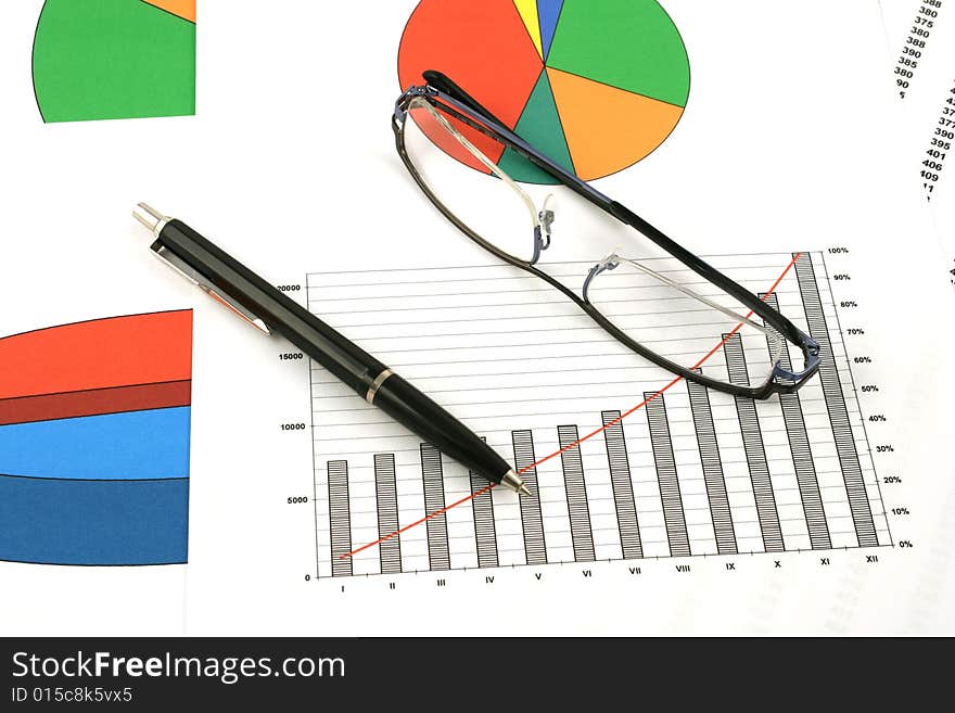 Ballpoint pen and glasses on earning graphs