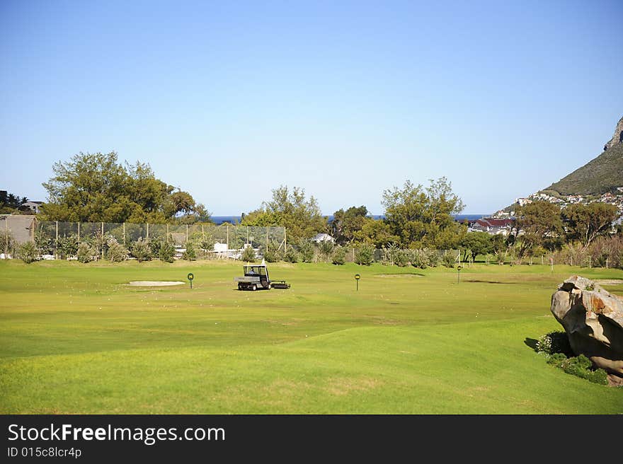 A beautifully maintained practice or driving range with distance markers for golfers to practice on. A motorized vehicle is in the process of picking up balls on the range. A beautifully maintained practice or driving range with distance markers for golfers to practice on. A motorized vehicle is in the process of picking up balls on the range.