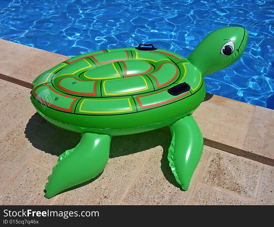 Green inflatable turtle on the edge of a swimming-pool. Green inflatable turtle on the edge of a swimming-pool