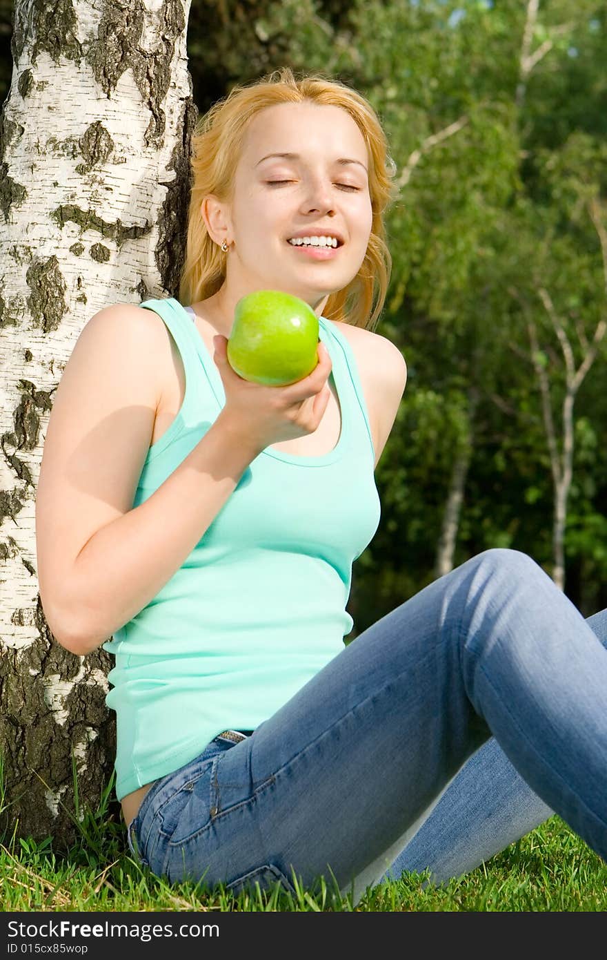 Pretty woman eating green apple on the summer glade