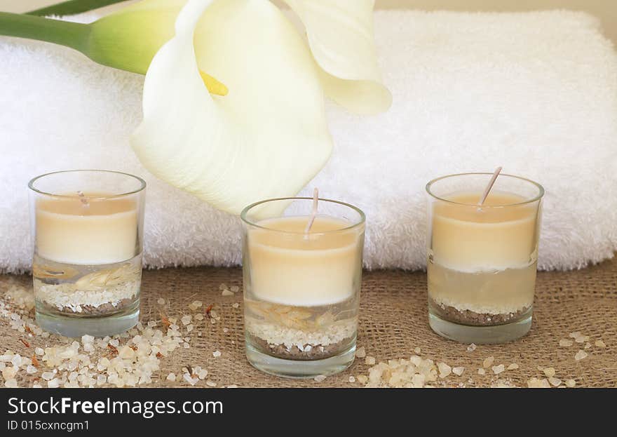 Relaxing spa scene with a white rolled up towel, white lillies, beautiful handmade candles and bath salts