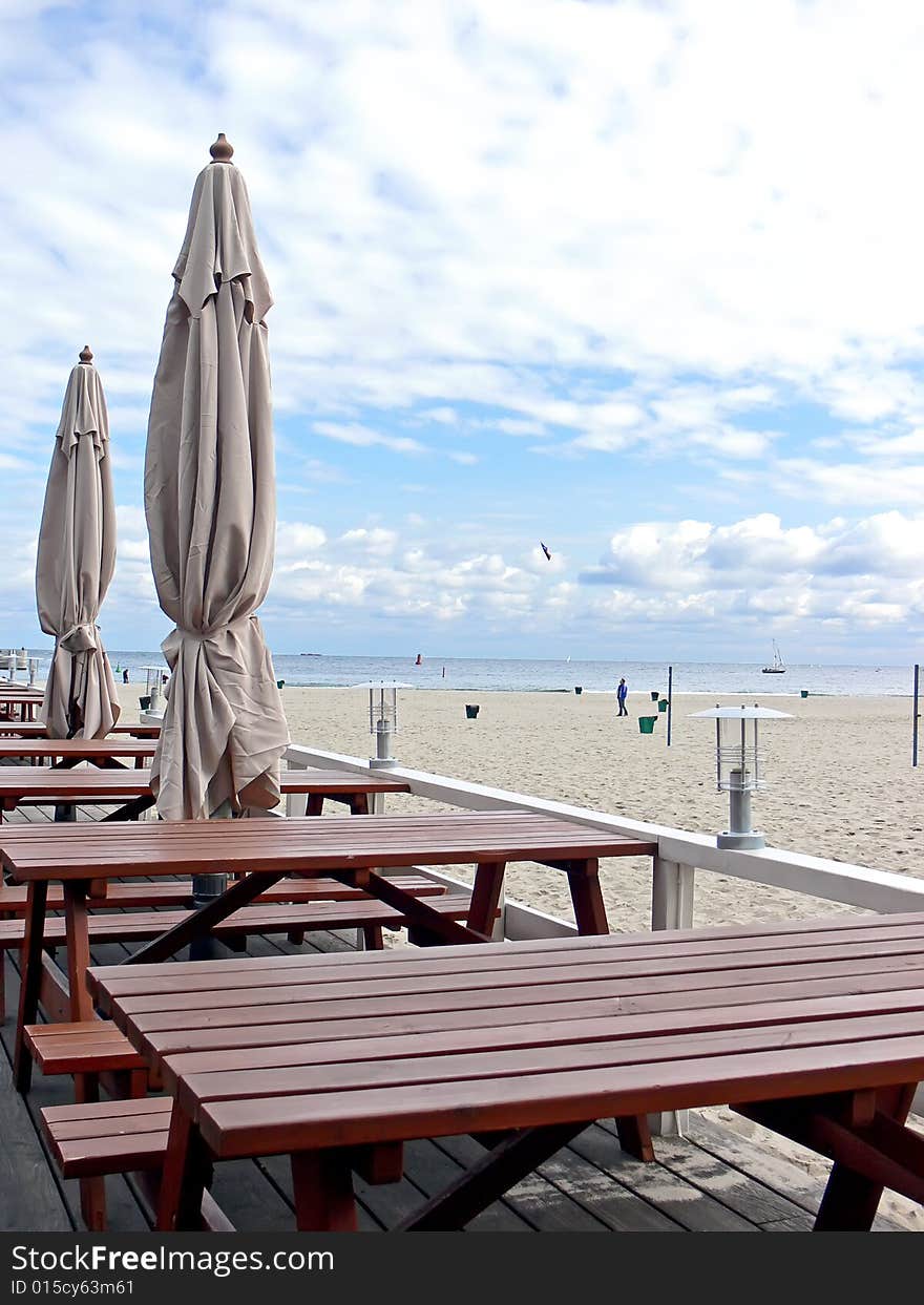 Wooden tables and umbrellas in outside restaurant with sea view.