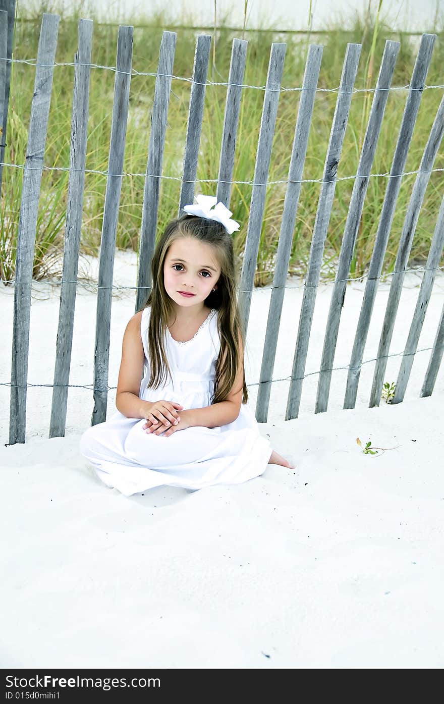 Pretty little brunette, brown eyed girl, dressed in a white dress, sitting on the beach in the sand. Pretty little brunette, brown eyed girl, dressed in a white dress, sitting on the beach in the sand.