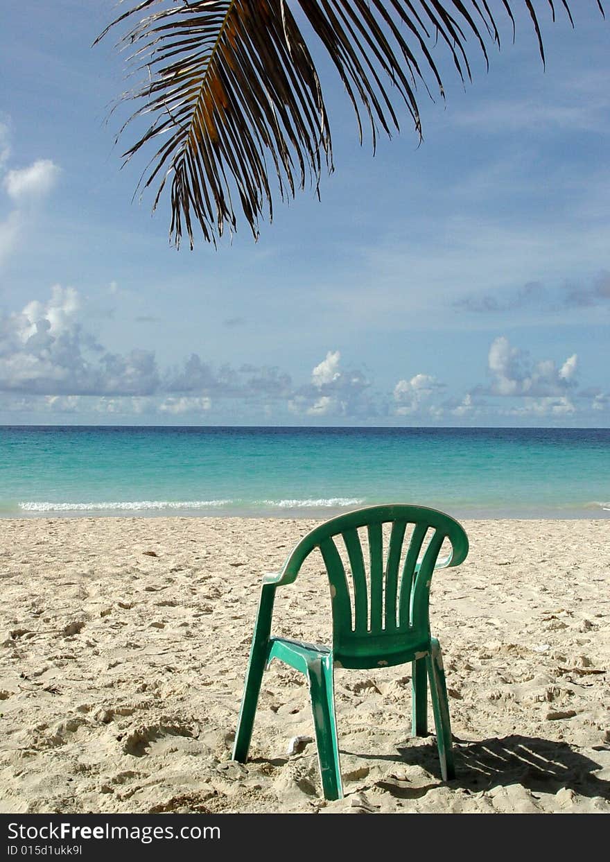 Green beach chair under a palm tree on the ocean shore in tropical resort, Barbados. Green beach chair under a palm tree on the ocean shore in tropical resort, Barbados