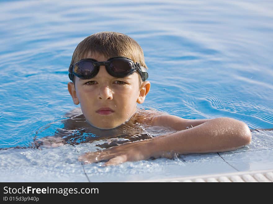 A boy holding in the side of a swimming pool with goggles. A boy holding in the side of a swimming pool with goggles