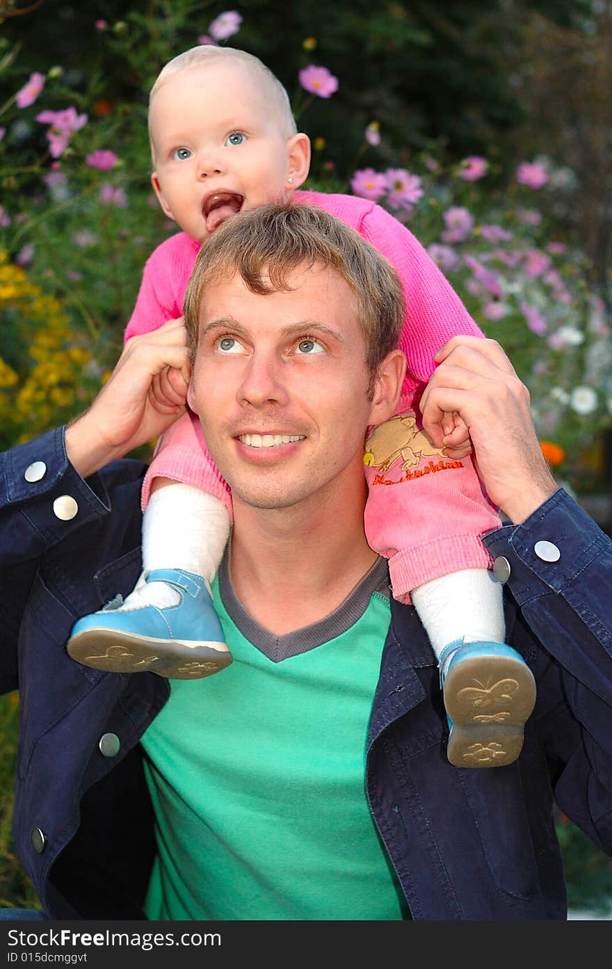 Proud father with his happy daughter sit on father's shoulders on flowers background. Proud father with his happy daughter sit on father's shoulders on flowers background.