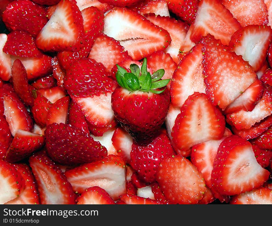 A pile of cut strawberries, with one whole one in the middle.