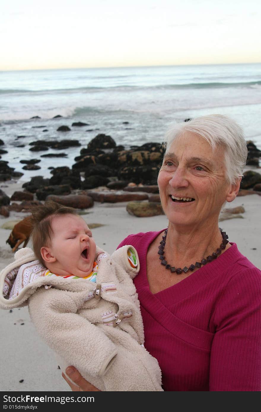 Grandmother with new granddaughter by the sea - family dog in the background. Grandmother with new granddaughter by the sea - family dog in the background