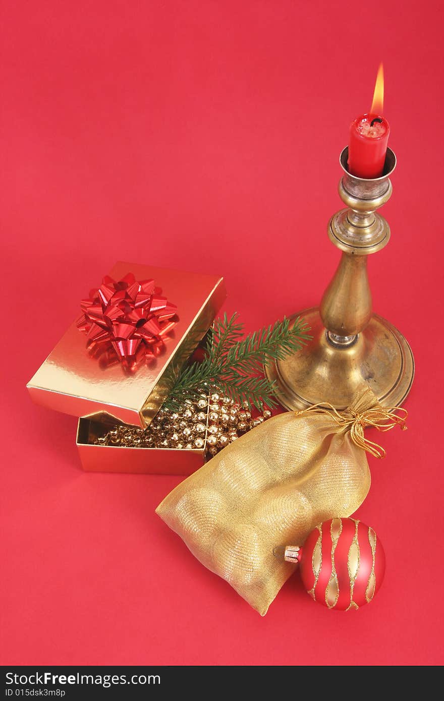 Christmas still life.Christmas candle with flame,present,christmas ball and tree.Red background.