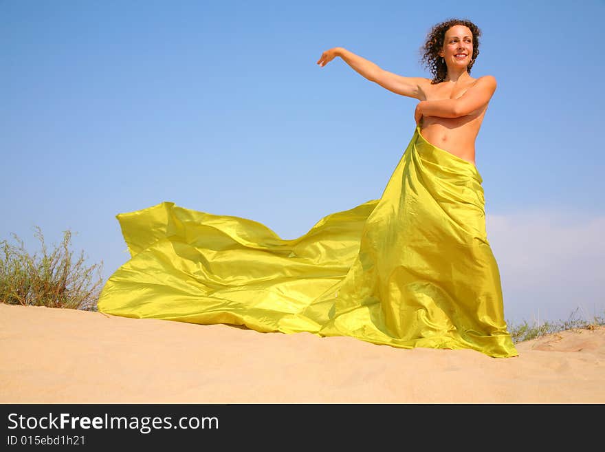 Naked woman with yellow fabric on sand