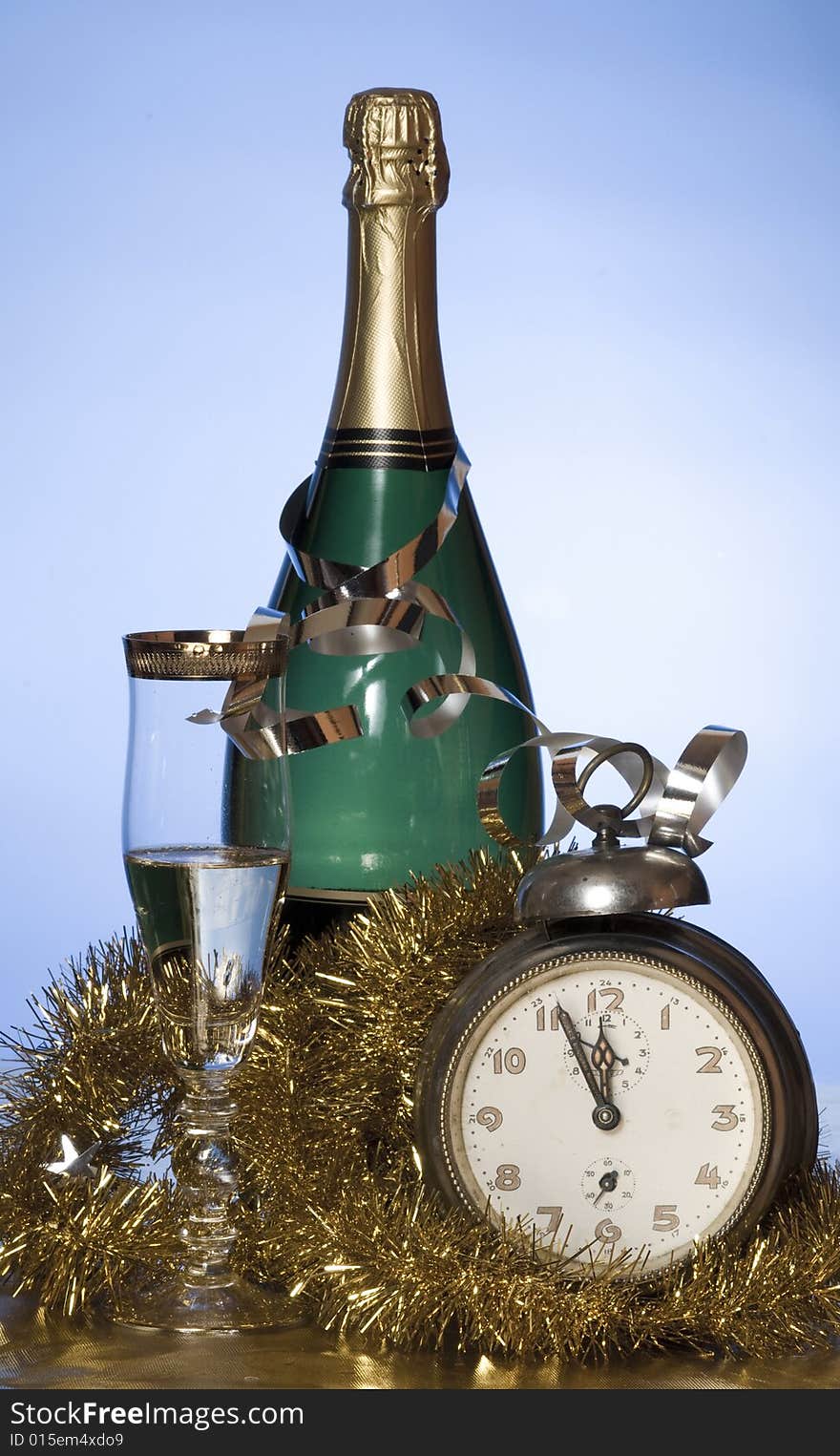 Champagne with glass, old alarm clock and golden decoration on blue