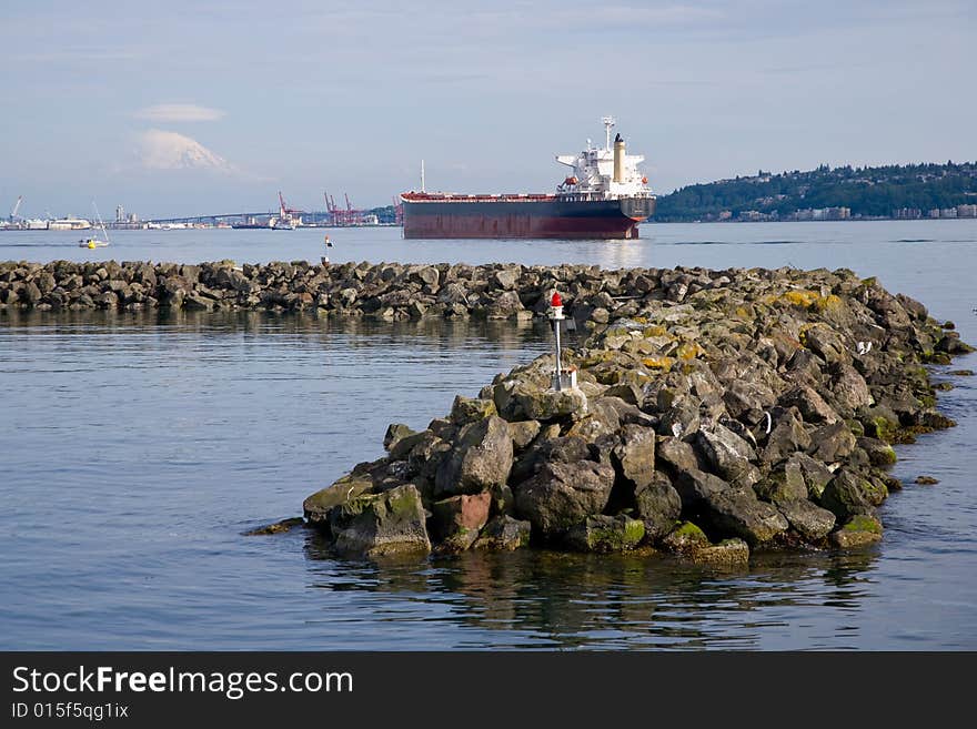 Seascape on Puget Sound of cargo ship and rock jetty, Mount Rainier in distance.