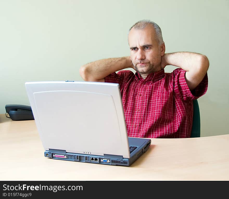 Thoughtful office worker working at the desk with laptop with hands on his neck