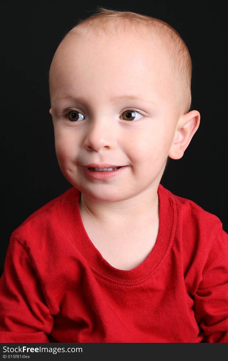 Blonde toddler against a black background with a  smile