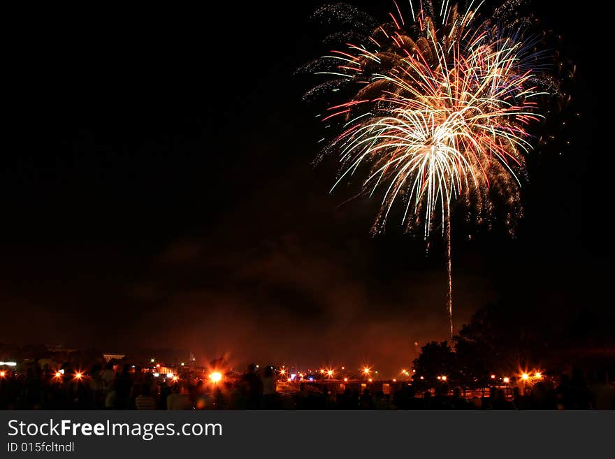 Downtown fireworks display. Time elapse image capturing multiple bursts. Silhouette crowd in the foreground with streetlights.