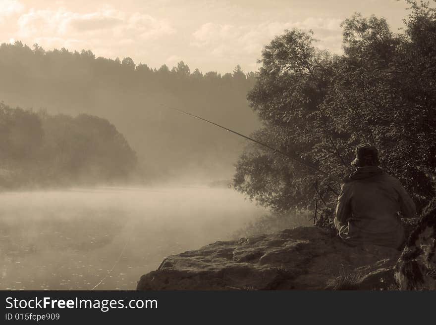 Lonely fisherman sitting on a bank of misty river. Lonely fisherman sitting on a bank of misty river