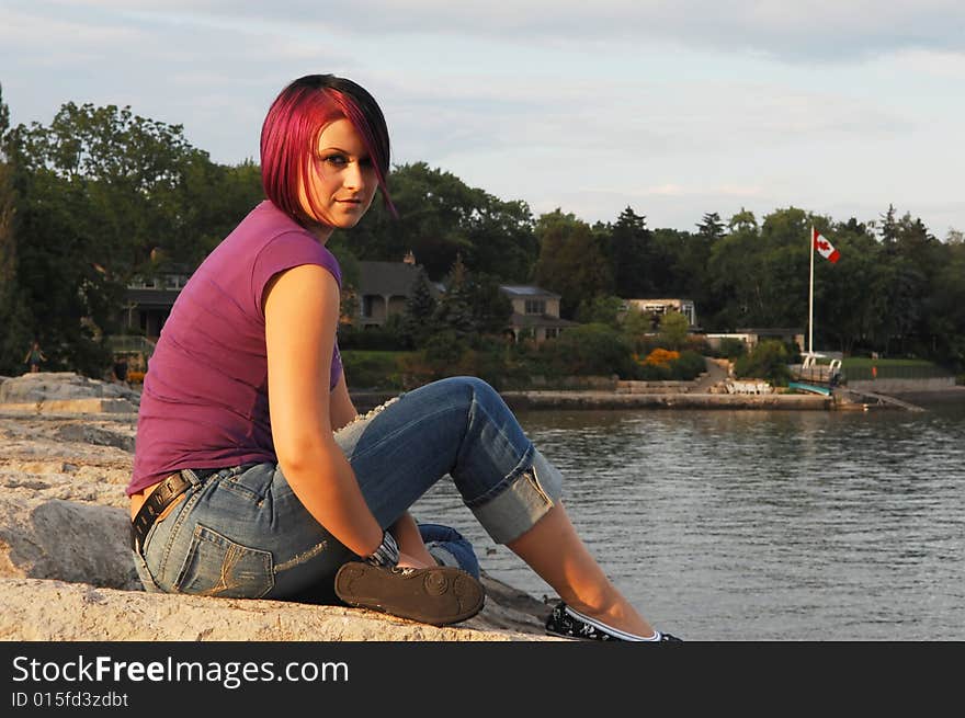 An red hair girl in jeans sitting on the shore of lake Ontario at sunset. An red hair girl in jeans sitting on the shore of lake Ontario at sunset.