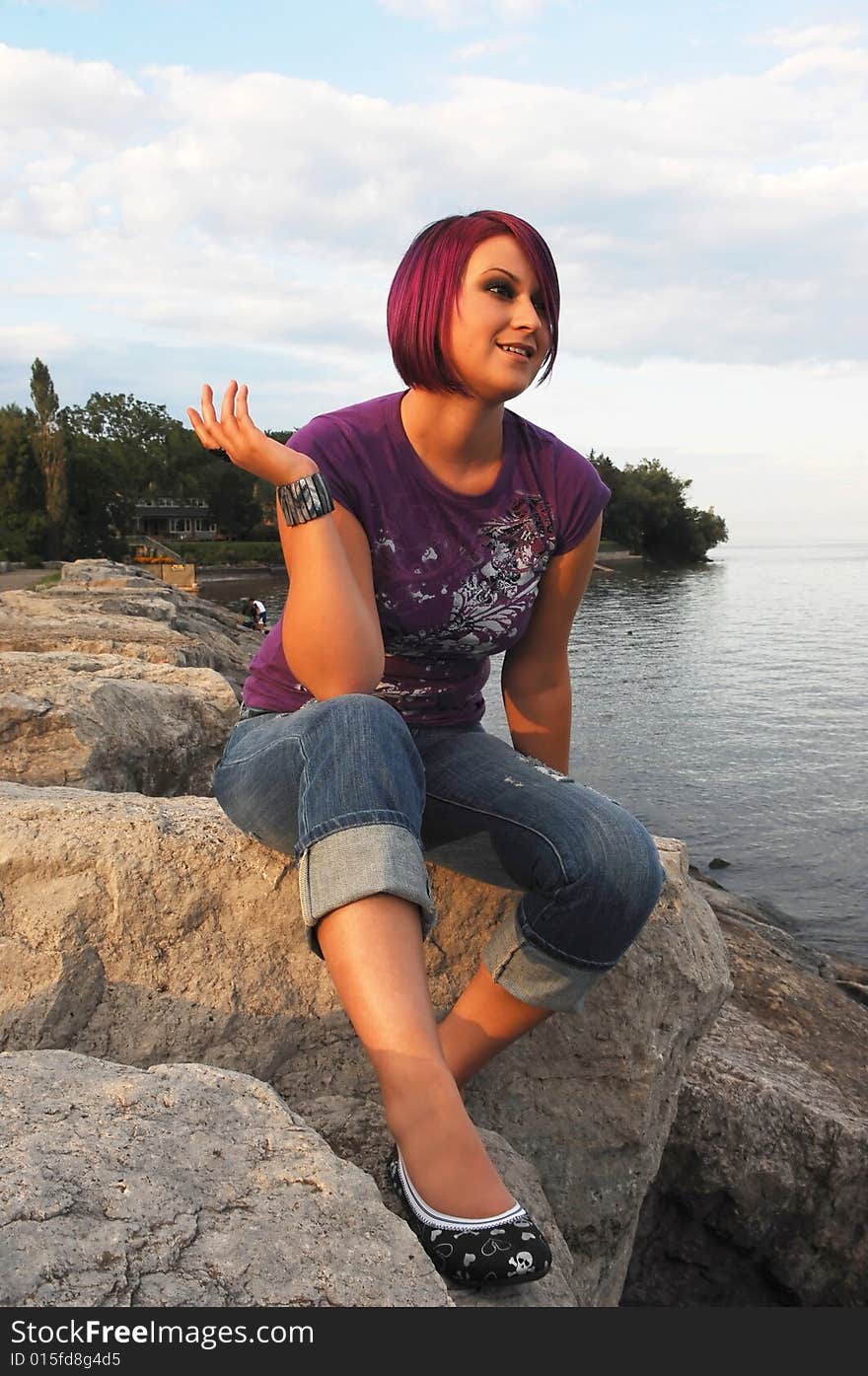 An red hair girl in jeans sitting on the shore of lake Ontario at sunset. An red hair girl in jeans sitting on the shore of lake Ontario at sunset.